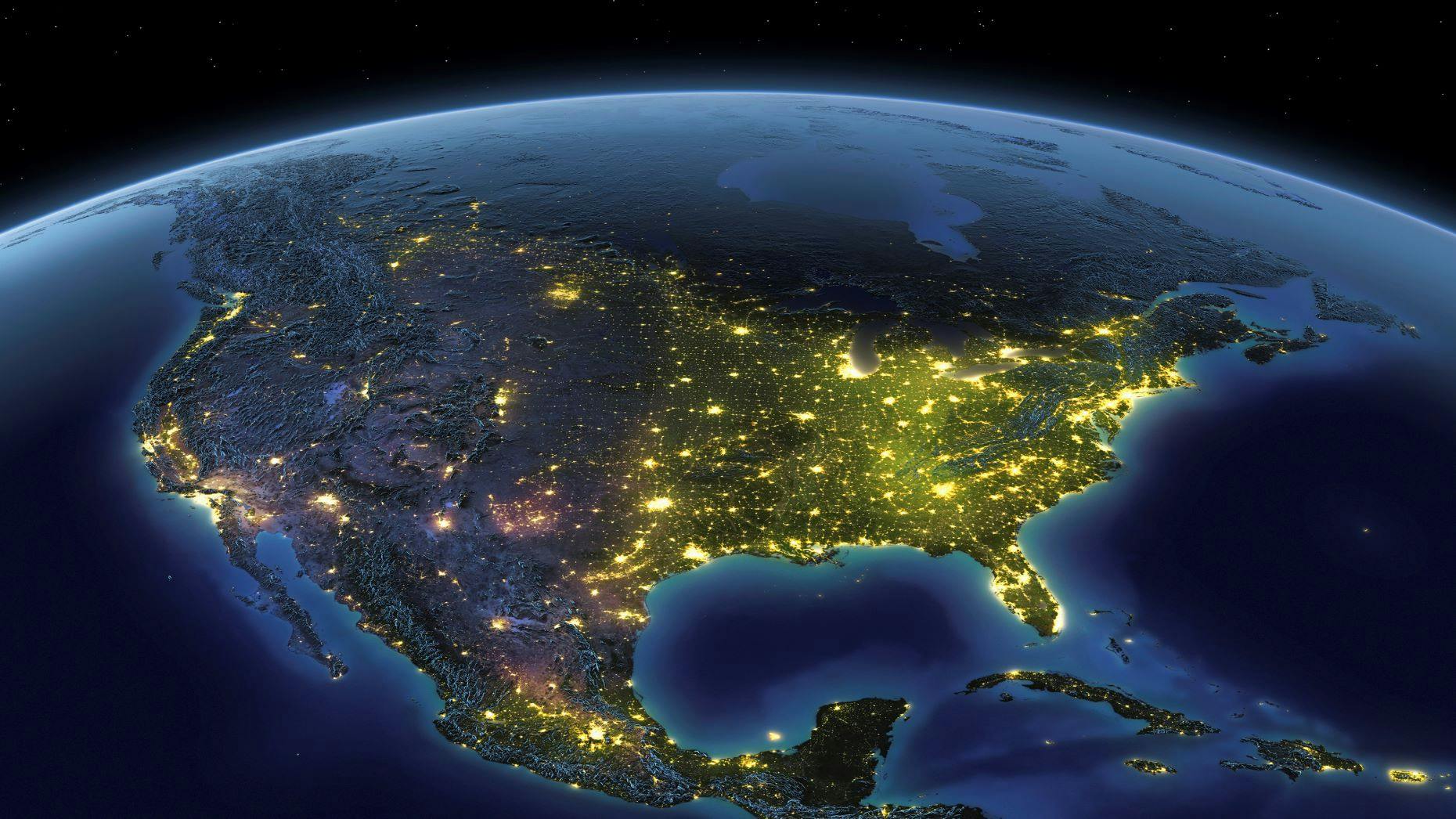 View of North America from space at night, showing illuminated city lights across the United States, Mexico, and Canada, with surrounding oceans and a dark, starry sky in the background.