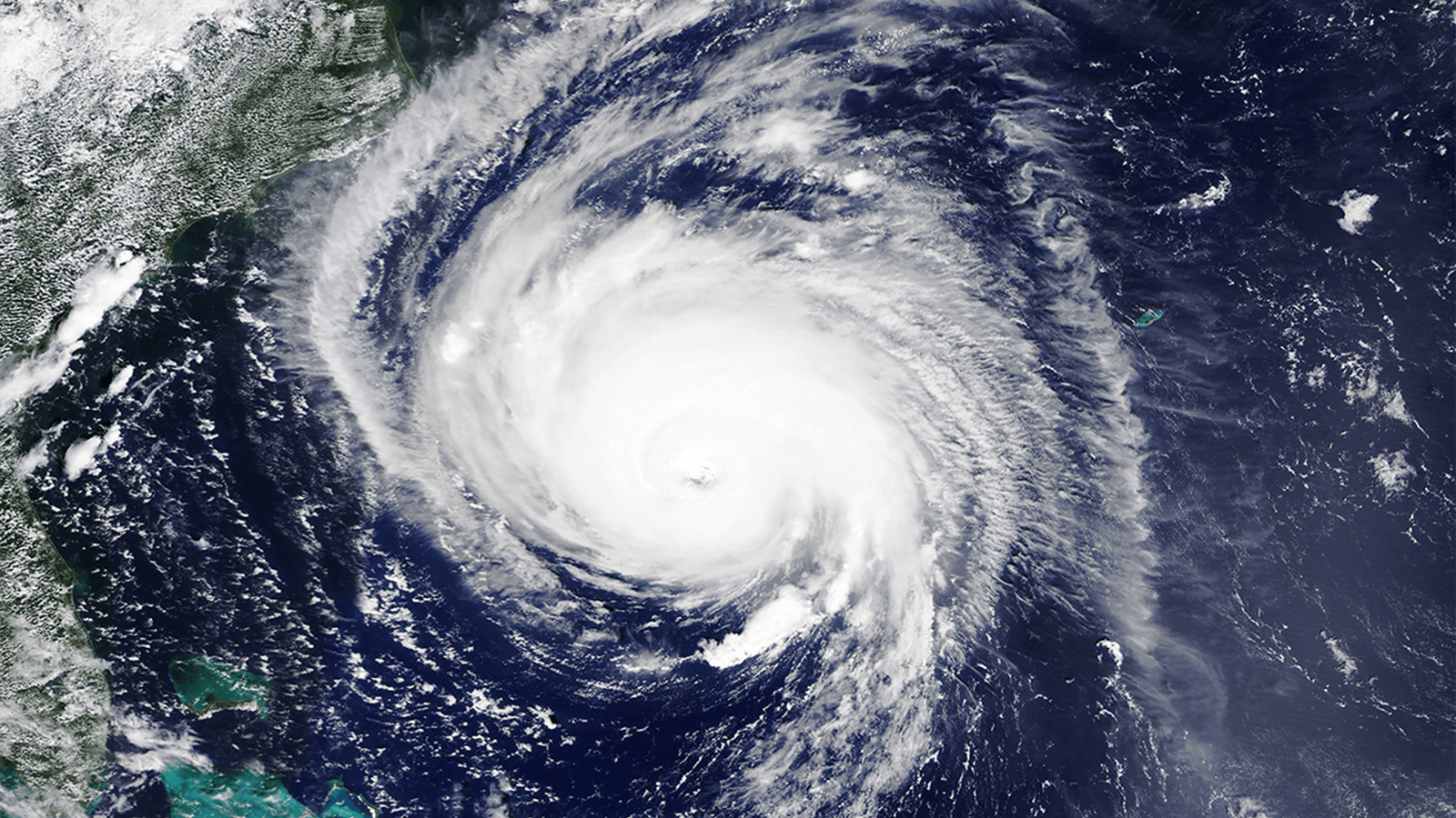 Satellite image of a large hurricane swirling over the Atlantic Ocean, with a well-defined eye at the center and thick white clouds spiraling outward, approaching the southeastern coast of the United States.
