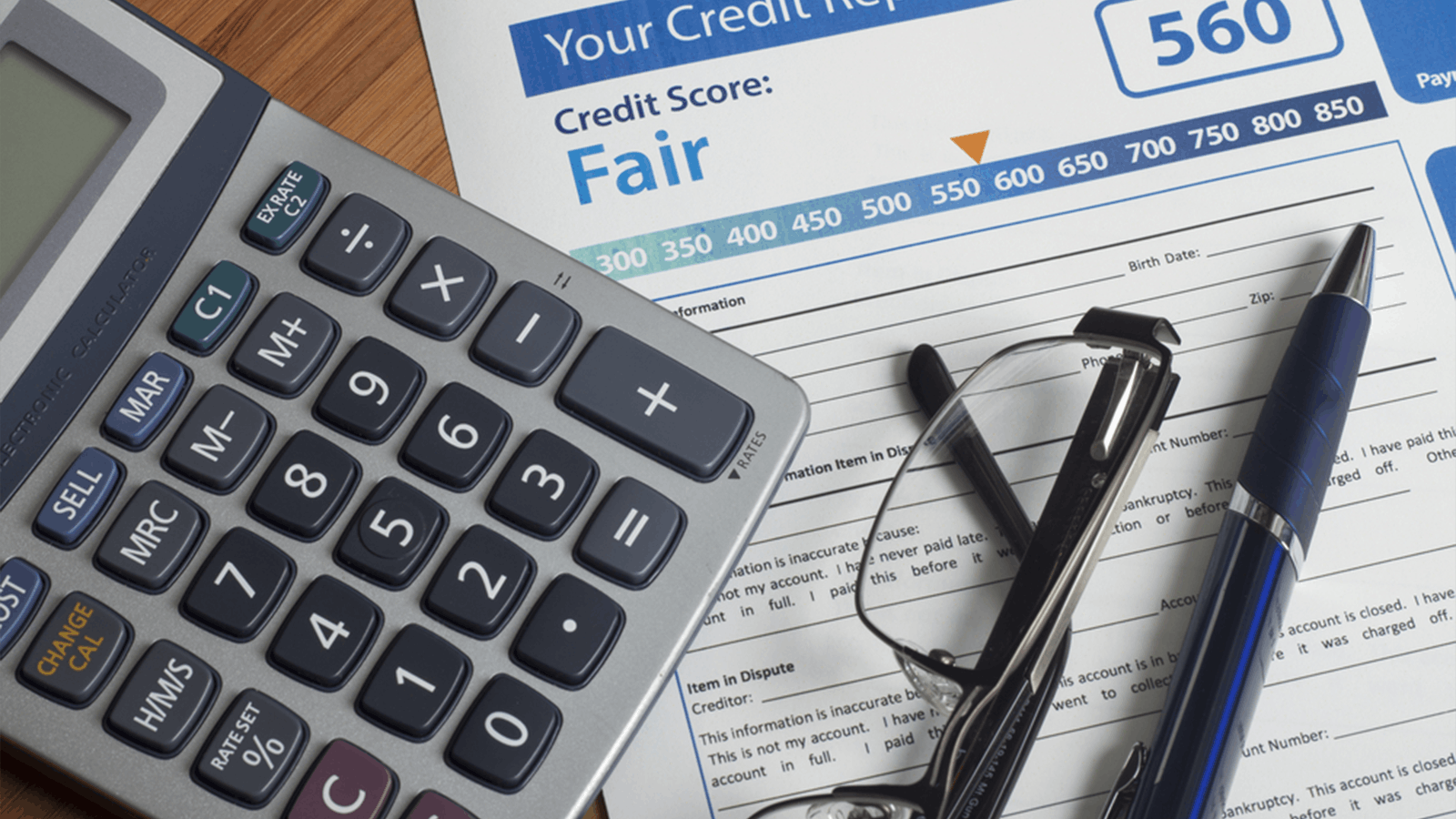 A close-up of a credit report showing a score of 560 labeled Fair, next to a calculator, eyeglasses, and a pen on a desk.