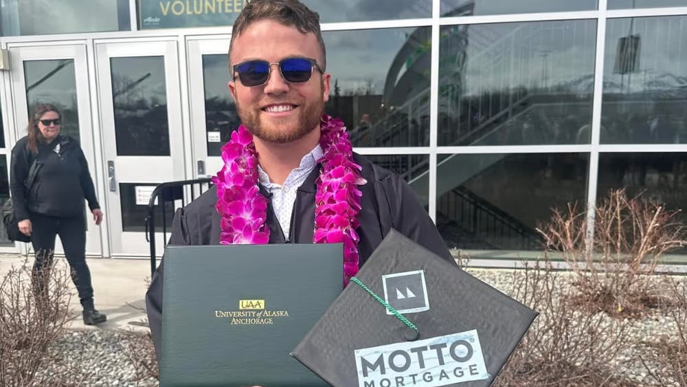 Lucas Adams wearing graduation robe and holding his diploma and mortarboard with the Motto Mortgage logo
