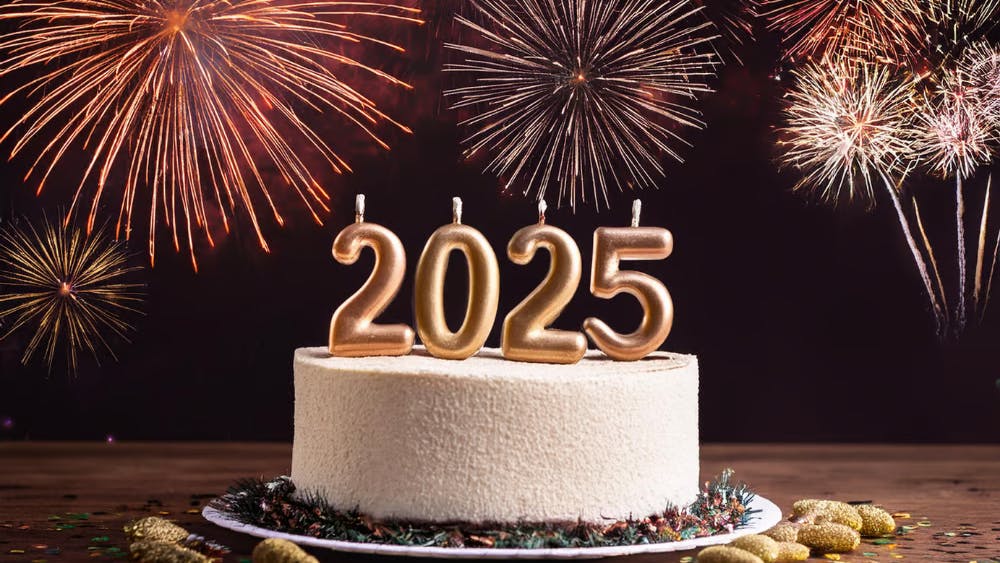 Image of a cake with "2025" candles and fireworks in the background.