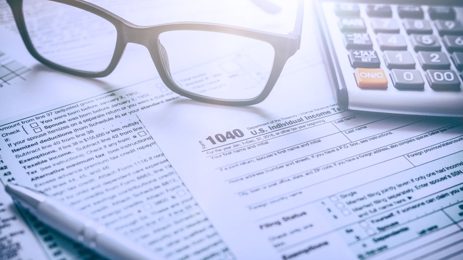 A close-up of tax forms, a pen, eyeglasses, and a calculator on a desk, suggesting tax preparation or financial planning.