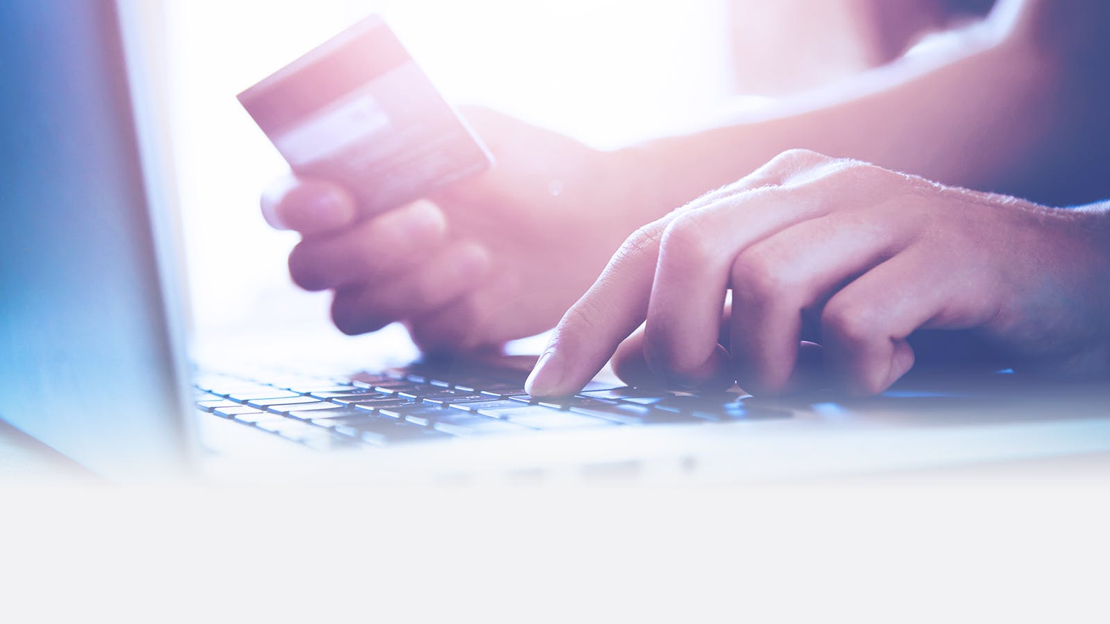 Close-up of a person holding a credit card in one hand while typing on a laptop keyboard with the other hand, suggesting online shopping or electronic payment.