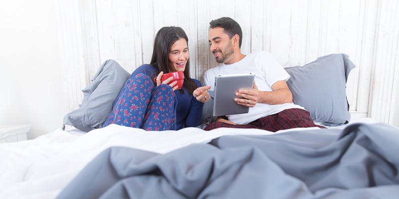 A photo of a coule sitting in bed and reviewing their home renovation budget on a tablet.