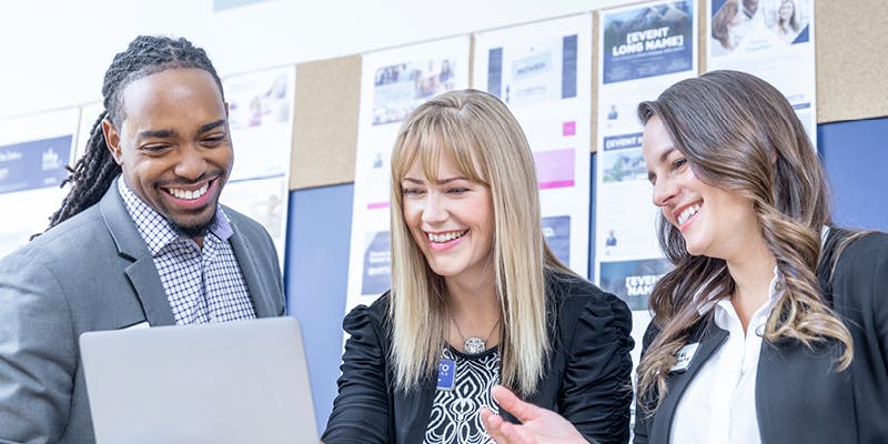 A team of employees working at a mortgage brokerage franchise. They are looking at a laptop and smiling.