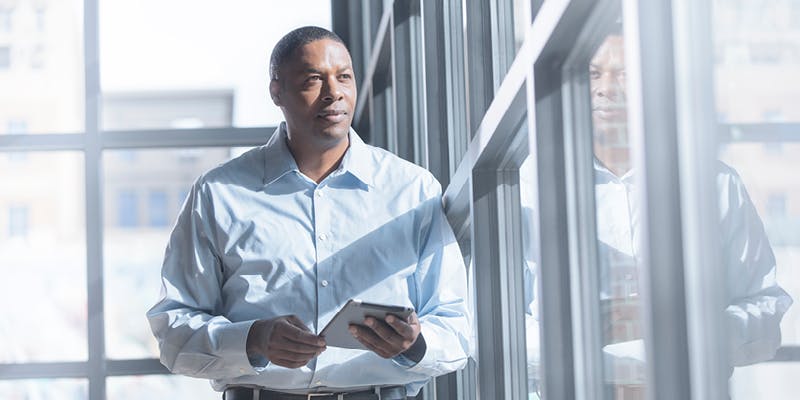 A franchise owner standing by a winder with a tablet, thinking about how to market his business.