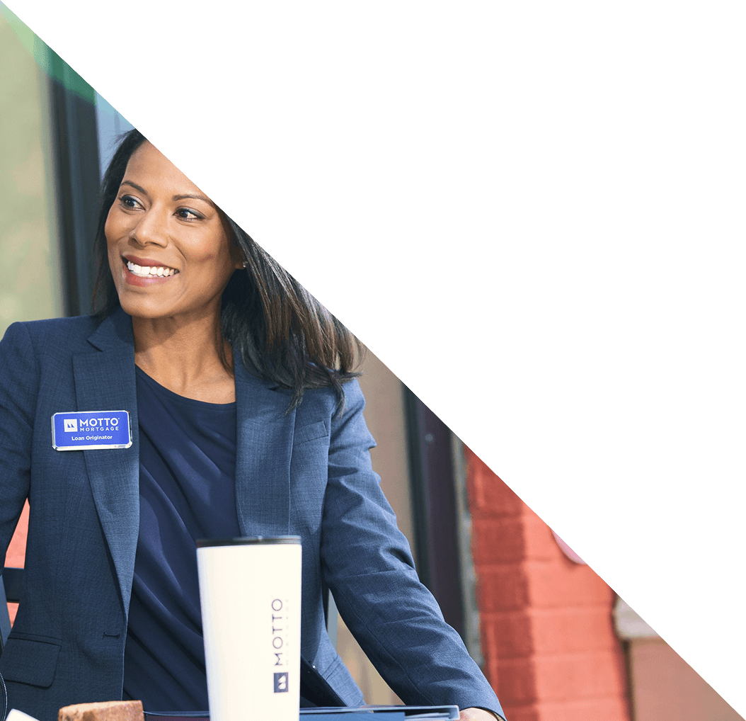A woman in a navy blazer with a Motto Loan Originator name tag smiles while sitting at a table with a white Motto cup. The top half of the image is covered by a white triangle.