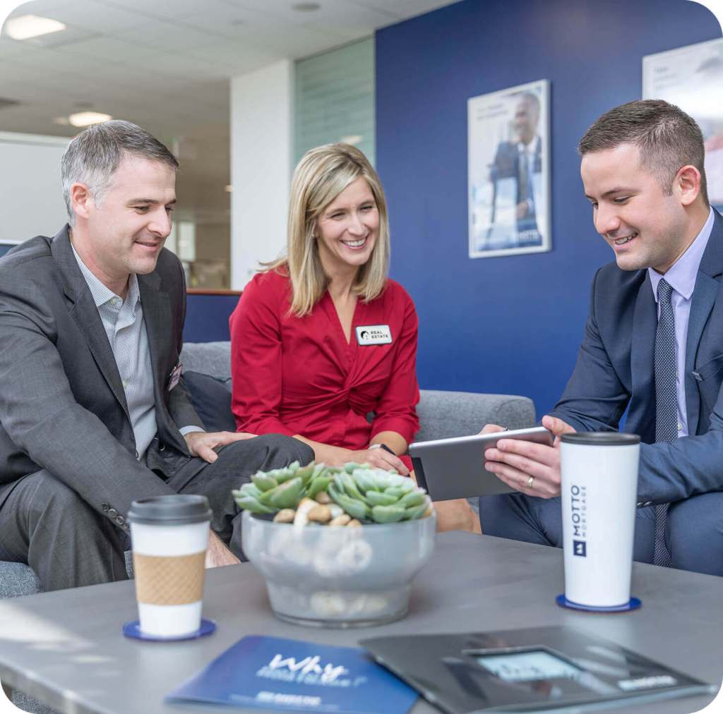 Why Choose Francise (1) 2 Three professionally dressed people sit on a gray couch in a modern office, smiling and looking at a tablet. Coffee cups, a plant, and paperwork are on the table in front of them, with blue walls in the background.