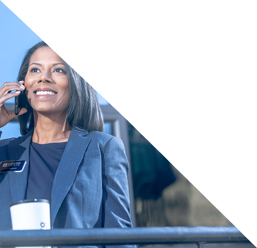 FranchsieHero A woman in a blue suit smiles while talking on a phone. She stands next to a railing with a coffee cup in front of her. The top part of the image is covered by a white triangular overlay.