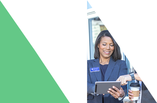 Top triangles A woman in a suit holds a tablet and smiles while another person points at the screen and holds a coffee cup; geometric green and white shapes frame the left side of the image.