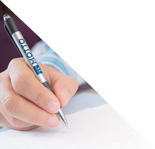 A person holding a pen labeled MOTTO is writing on a sheet of paper, with the image background partially faded to white.